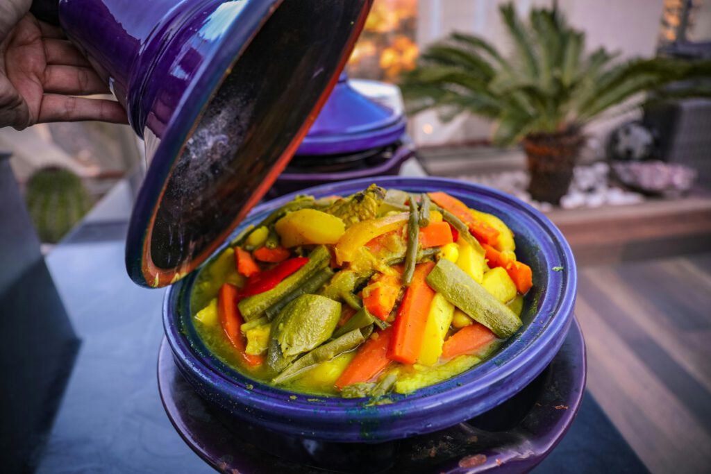 traditional moroccan tajine served in purple ceramic pot with a lid, filled with vegetables such as carrotts, courgette, potatoes and more
