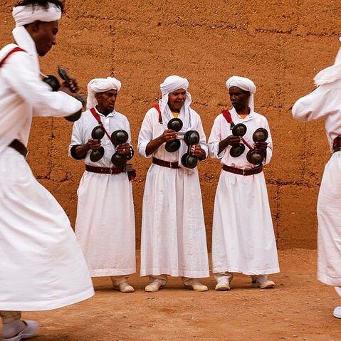 traditional morroccan men dressed in white dancing and performing music with metal castagnettes in the desert