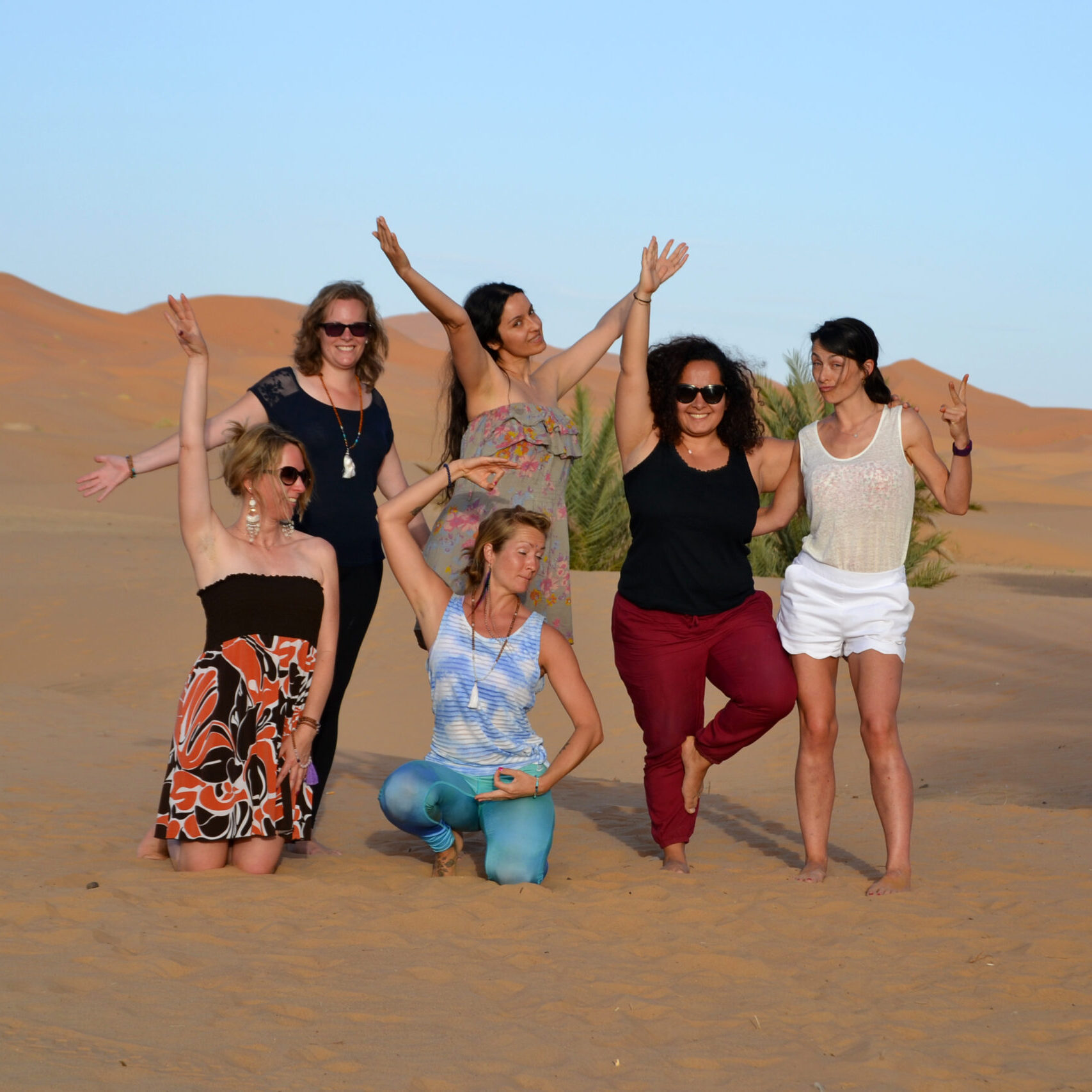 group of women in the sahara desert morocco at desert u retreat, posing for a picture happy, arms up in the air