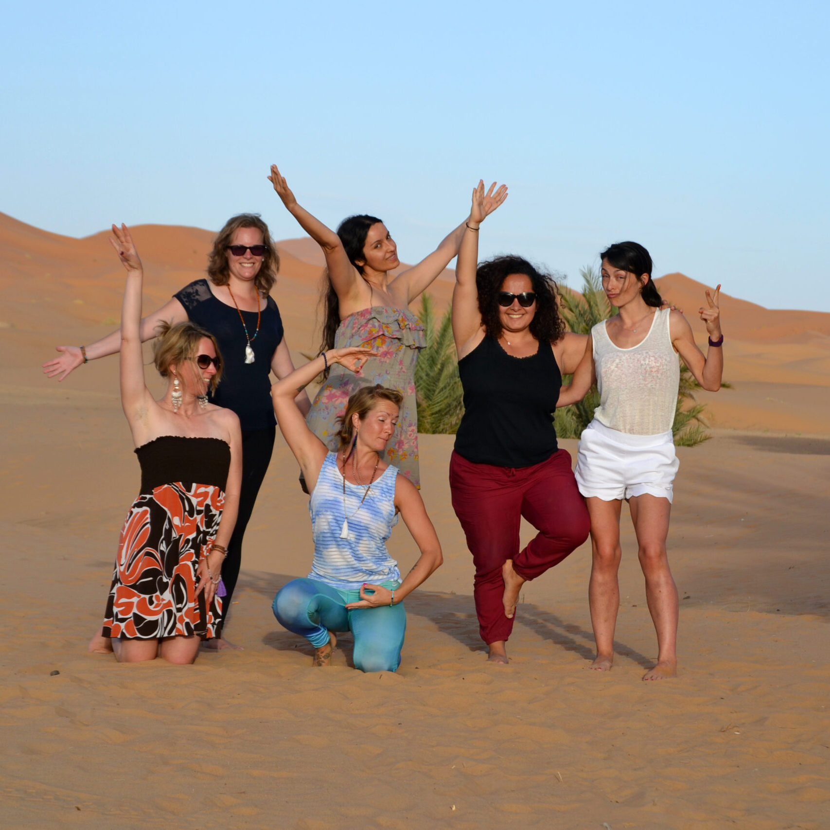 group of women in the sahara desert morocco at desert u retreat, posing for a picture happy, arms up in the air
