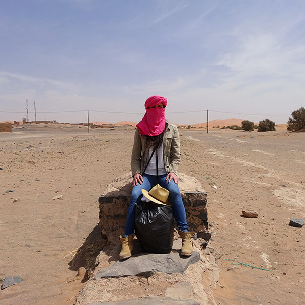 owmen wearing a pink scarf sitting on a stone in the desert, desert retreat