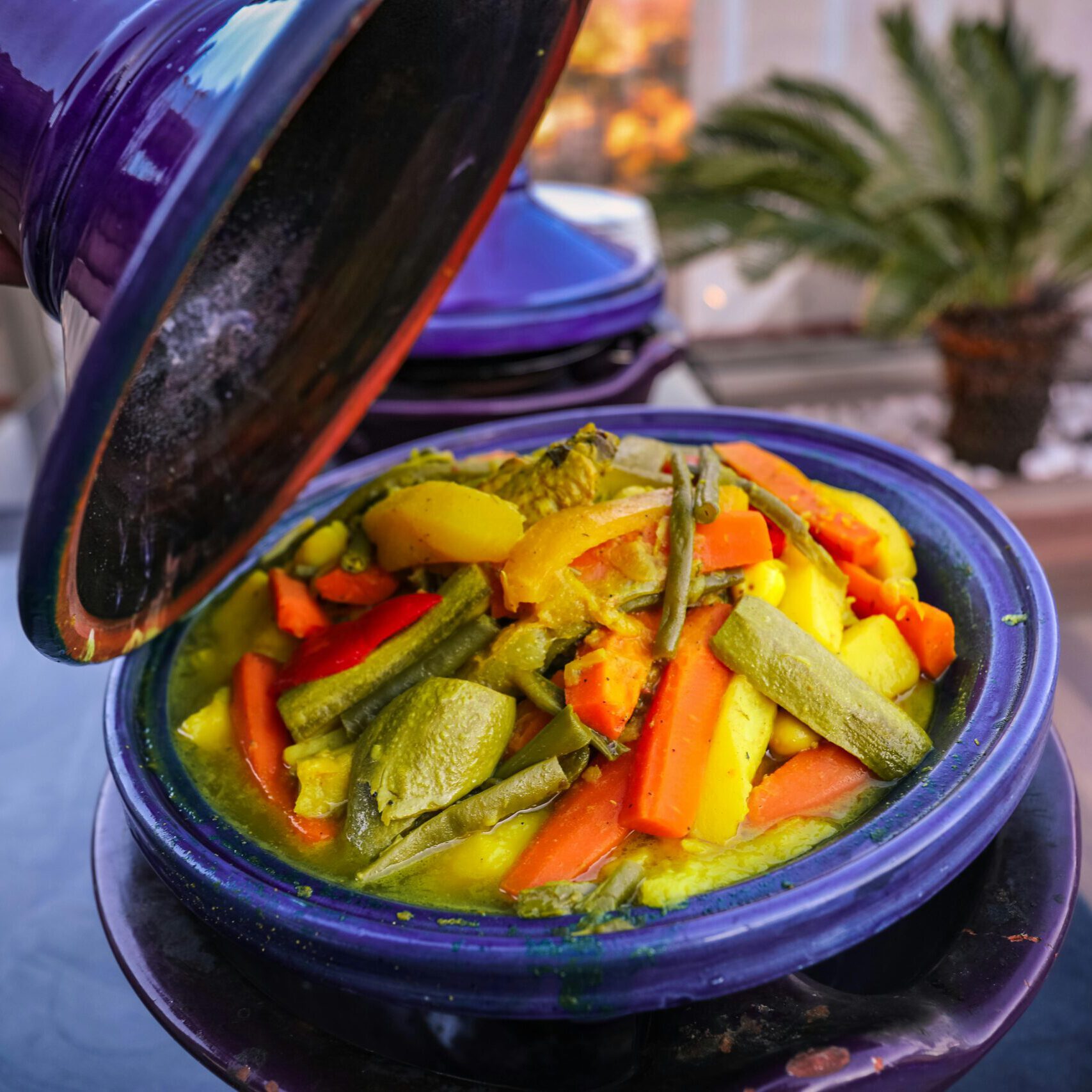 traditional moroccan tajine served in purple ceramic pot with a lid, filled with vegetables such as carrotts, courgette, potatoes and more