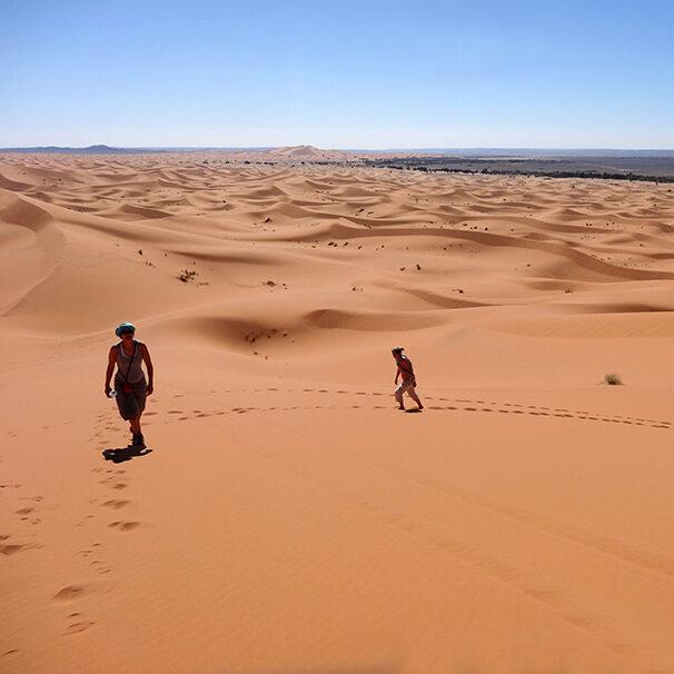 three woman walking up a high dune n the sahara dsert, morocco, on a retreat