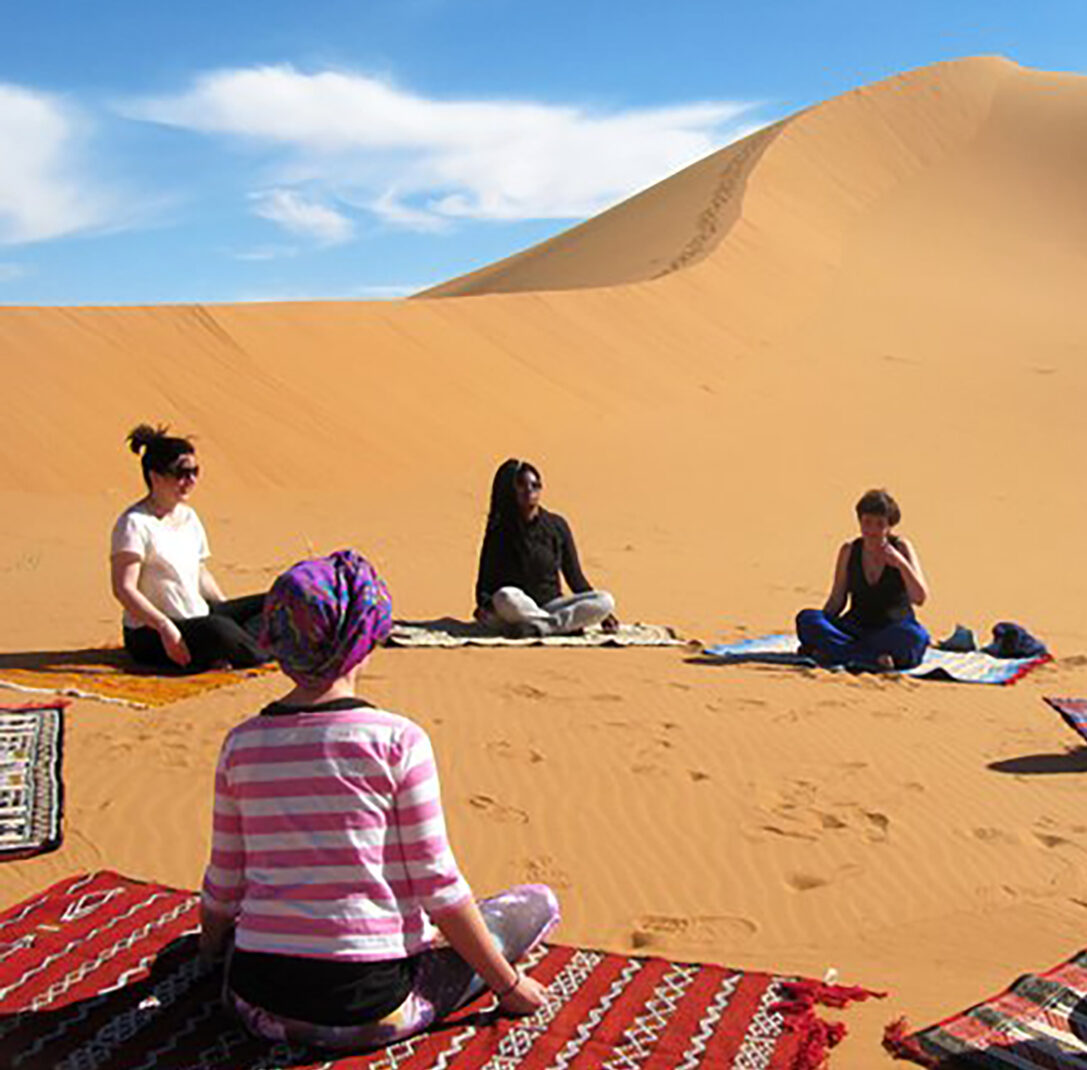group of owmen in the sahara desert sitting on carpets in meditation