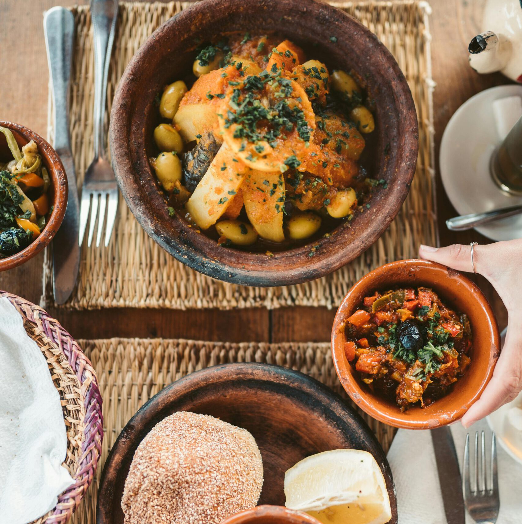traditional moroccan food, such as tajine, round bread, antipasti with olives set on a table in ceramic pots, seen from above