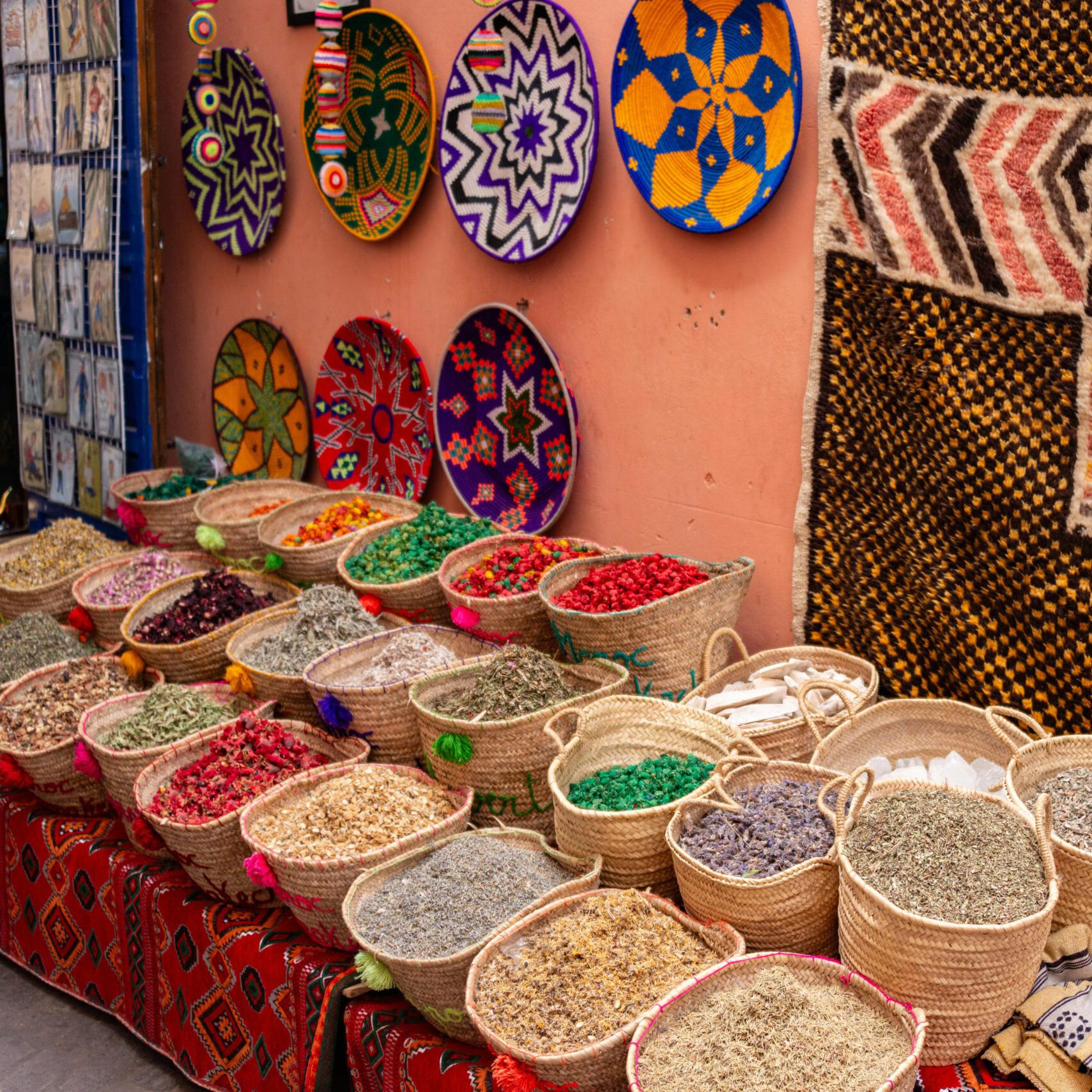 morroccan shop with colorful herbs in baskets, colorful handmade plates of natural material on wal, and carpets