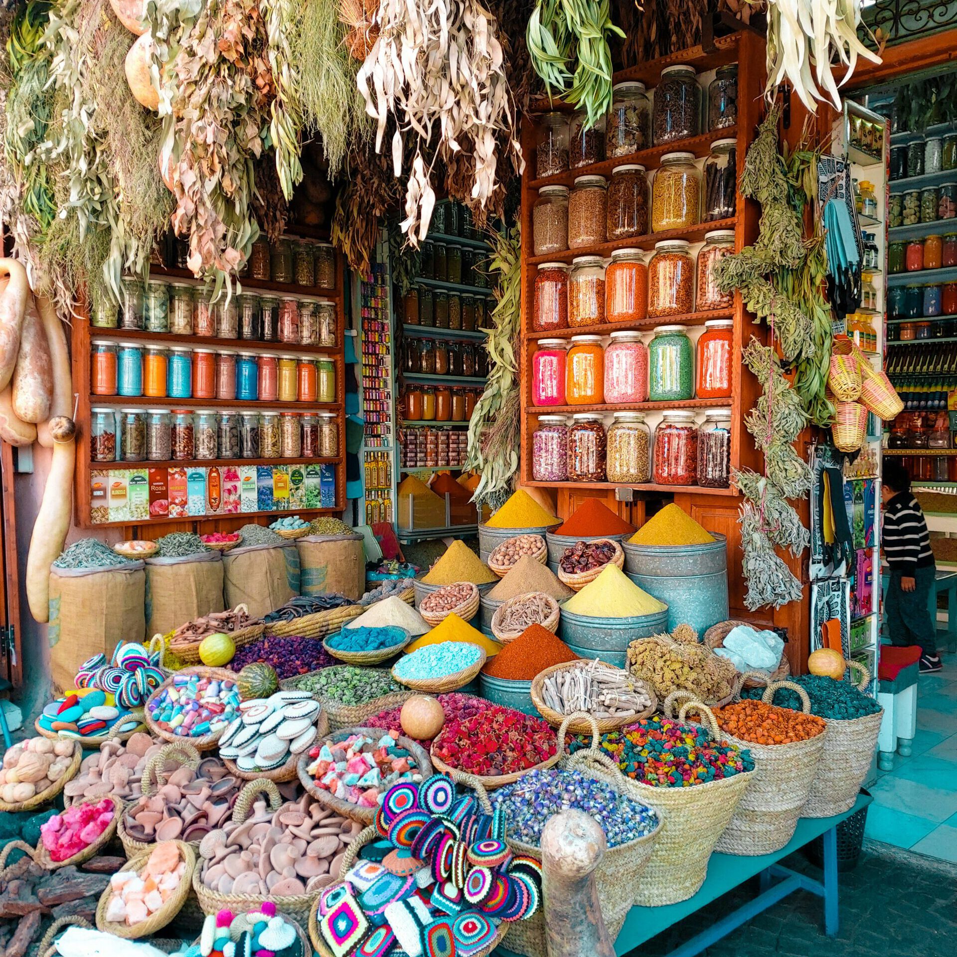 a shop in a traditional souk (bazaar) in morocco with a lots of colorful things, such as open baskets with herbs, soices, and glasses filled with colorful spices, morrocco