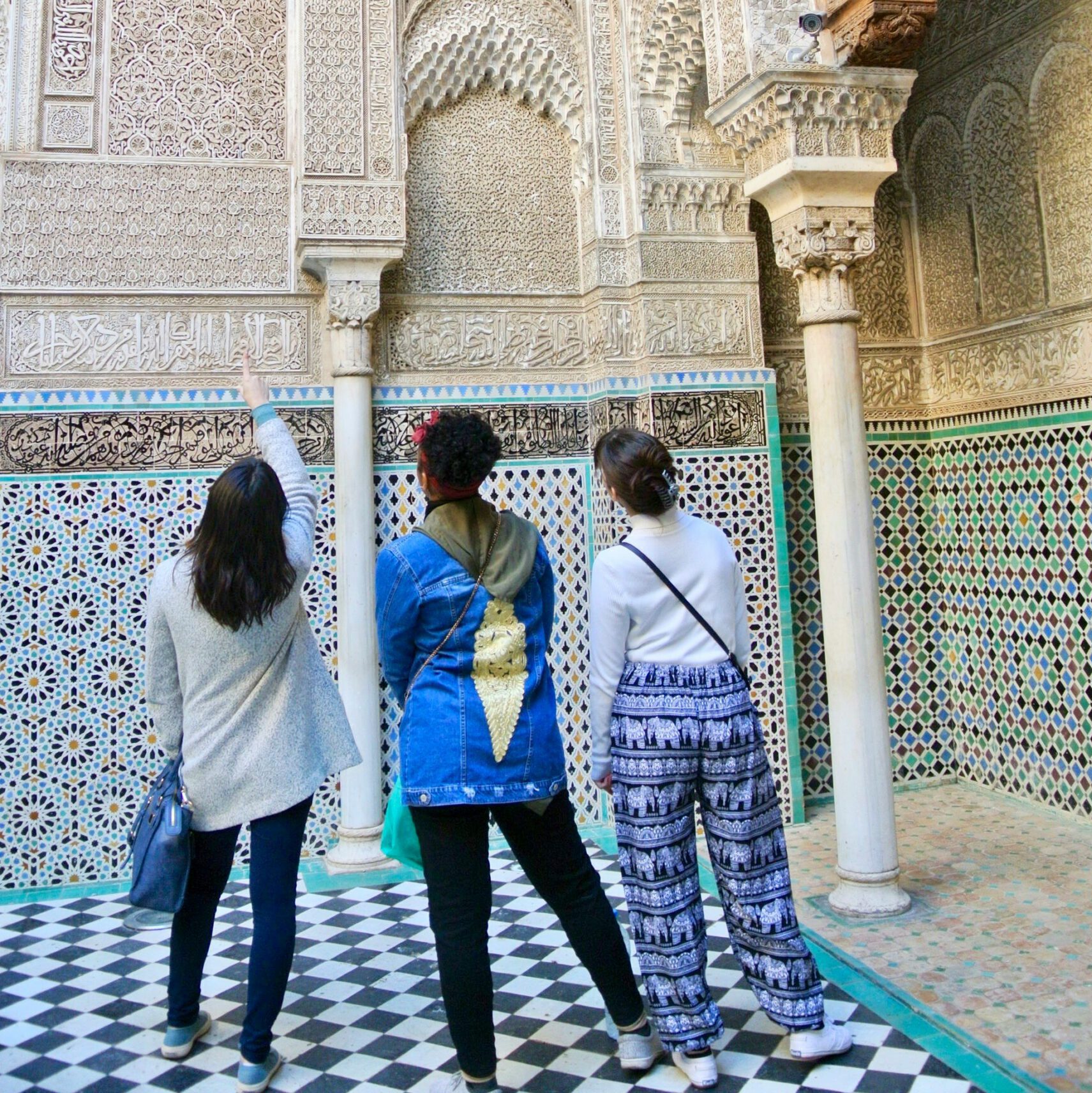 three women seen from behind standing in a traditional moroccan building with stucco and tiles