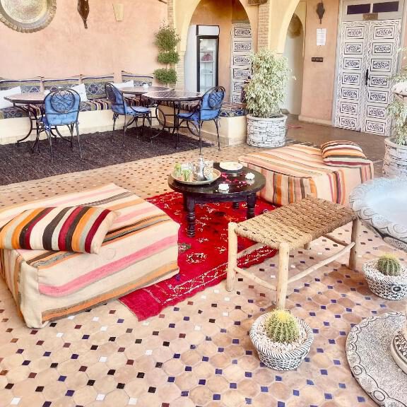 terrace of a riad in marrakesh with puffs, low tables, carpets, and decoration on the walls
