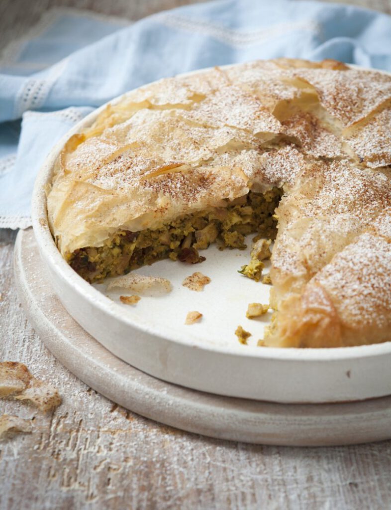 Moroccan pastilla dish, with flaky crust outside and meat and vegetable filling inside, and icing sugar and cinnamon on top