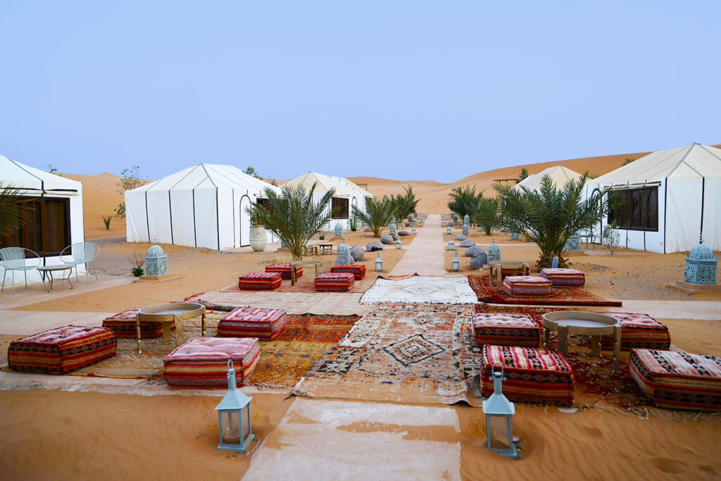 desert luxury camp with 3 white tents on both sides and red pillows on the ground in the middle