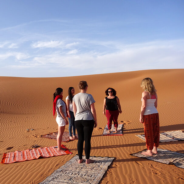 women standing in a circle in the sahar desert for yoga, meditation, dance, morocco